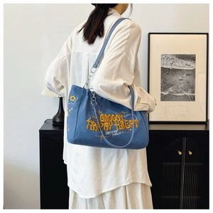 Blue canvas tote bag with colorful embroidery shown on model in a modern home setting