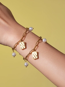 Detailed view of two gold stainless steel bracelets with checkers charms and white pearls