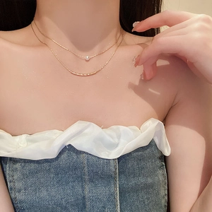Detail of double-layer gold chain necklace with white pearl and curved metal bar pendant