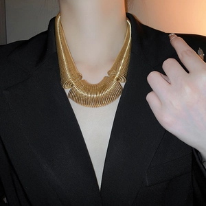Detail view of bold chunky gold spring coil necklace on model with black suit