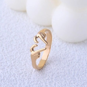 Detailed close-up of a gold heart-hand gesture ring on a minimalist white surface