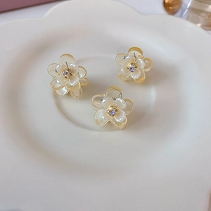 Detail of three mini cream floral hair clips with pearl finish and rhinestones in a tray