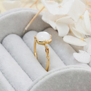 Macro shot of gold shell ring with white oval stone in a gray velvet jewelry box