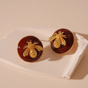Detail view of round red enamel bee earrings with gold finish on a white stone tray