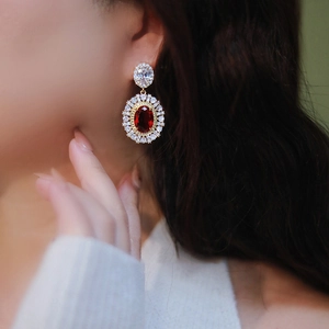 Elegant drop earring with oval red gemstone and white zircon halo worn by a model