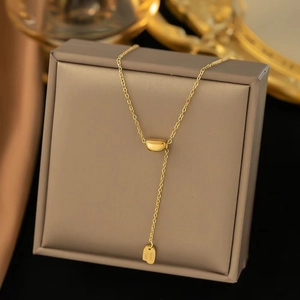 Macro detail of 18K gold plated titanium necklace with tassel pendant and engraved tag