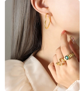 Detail of model wearing twisted gold hoop earrings and an emerald gemstone ring set