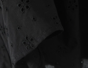 Gros plan du tissu noir de robe avec broderie florale délicate et détails ajourés