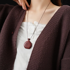 Detail of a dark red wooden gourd pendant on a black cord necklace worn by a model