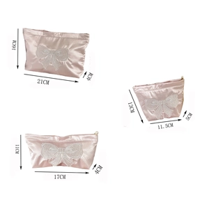 Three sizes of pink satin cosmetic bags with bow embroidery and pearl zipper detail