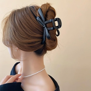 Detail of a large black glossy bow hair claw clip styled in a modern bun for women