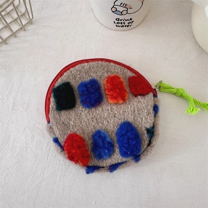 Close-up of a round plush makeup bag with colorful polka dots and a green zipper pull