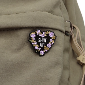 Détail d'un badge en cœur avec rose Shut Up épinglé sur un sac à dos en toile