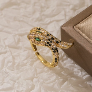 Detail of gold snake ring with black and green zircon stones on white paper background