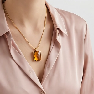 Close-up of model wearing amber square glass pendant on golden snake chain necklace