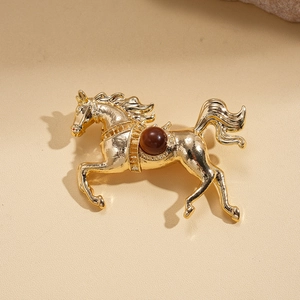Detailed view of horse-shaped brooch in gold finish with brown bead and saddle texture