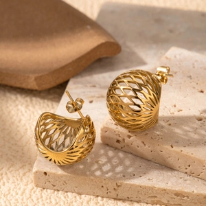 Elegant gold hollow mesh sphere earrings on natural stone background with metallic luster