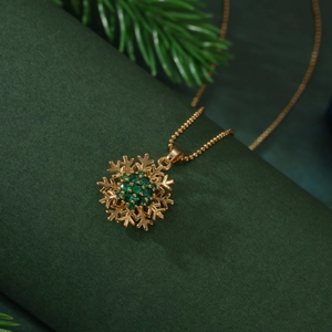 Rotating golden snowflake necklace with green zircon crystals on a pine needle background