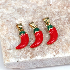 Three red enamel chili pepper charms with golden loops on pink stone background