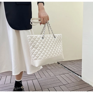 Detail of white quilted tote bag featuring silver-tone chain and woven leather straps