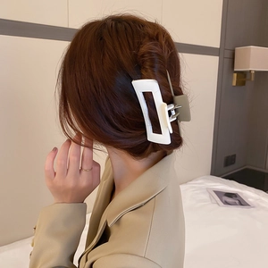 Détail d'une grande pince à cheveux géométrique blanche portée sur les cheveux d'une femme