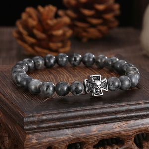 Macro shot of men's beaded bracelet with stone beads and silver skull cross pendant