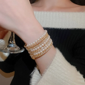 Detail of multilayer pearl bracelet with rhinestones worn while holding a glass