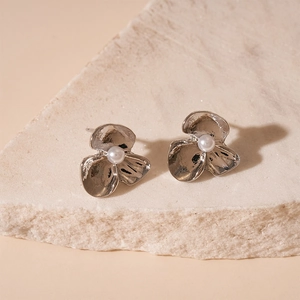 Detailed macro of silver flower stud earring with pearl accent on textured stone