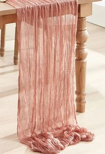 Detail of rose pink wrinkled gauze table runner draped over a natural wood table