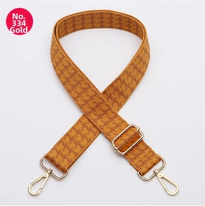 Detail of adjustable wide bag strap with brown and orange houndstooth weave and gold hooks