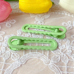 Detail of two green wavy hair clips on white lace with tulips in a soft natural setting