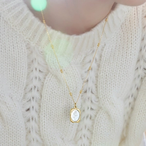 Gold rose pendant necklace with mother of pearl inlay on white knit sweater