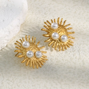 Detail view of 18K gold sunburst stud earrings with pearls on white stone surface
