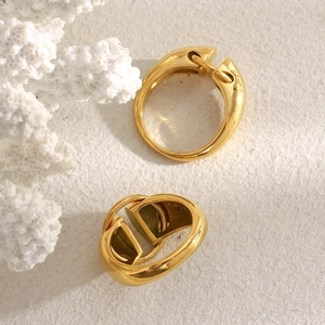 Detail of 18K gold-plated geometric D-letter ring on a textured cream surface