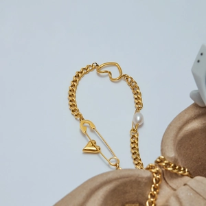 Dettaglio del bracciale a catena a graffetta dorata con ciondolo a cuore e perla bianca