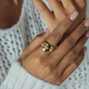 Détail d'une bague large en or avec trois perles portée sur un pull en maille douce