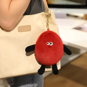 Close-up of a cute red plush peanut doll with golden metal keychain on a canvas bag