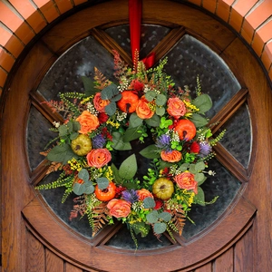 Autumn door wreath with orange roses, green pumpkins and red ribbon on a rustic wooden door