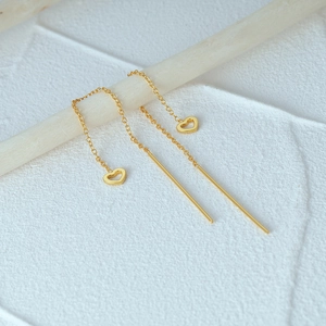 Macro detail of gold heart tassel threader earrings hanging on a wooden display stand