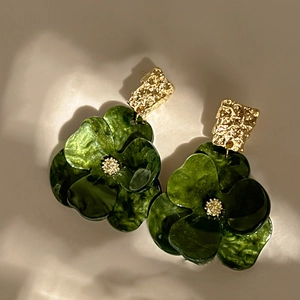 Macro shot of dark green acrylic flower earrings with textured gold metallic accents