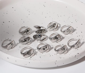 Close-up of twelve engraved stainless steel floral rings on a white ceramic plate