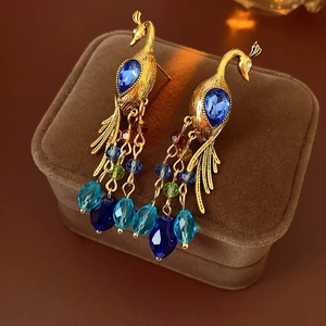 Detail of vintage peacock earrings with blue crystals and gold metal on velvet