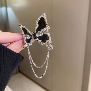 Détail d'une broche papillon argentée avec émail noir et franges en métal liquide