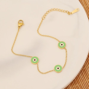 Macro shot of gold stainless steel bracelet with green evil eye charms on a ceramic plate