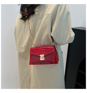 Detail of red crocodile pattern flap bag with gold chain and metal lock on beige coat