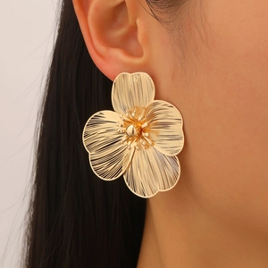 Macro detail of large gold flower earrings featuring a delicate wire-woven metal texture