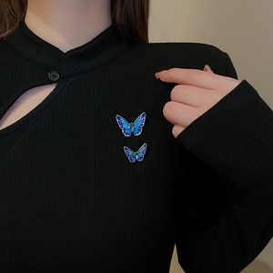 Detailed view of two gradient blue butterfly brooches worn on a black knit garment