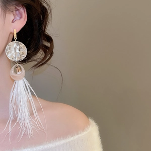 Détail de boucles d'oreilles bohèmes à pompons plumes blanches et disques de résine nacrés