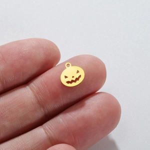 Detailed macro of gold pumpkin pendant with scary face cutout and top bail on finger