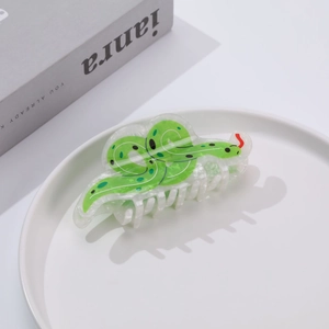 Detail of green snake-shaped acrylic hair claw clip with leopard spots on white plate
